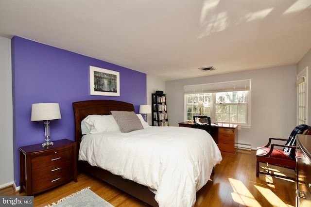 bedroom featuring hardwood / wood-style floors and a baseboard heating unit