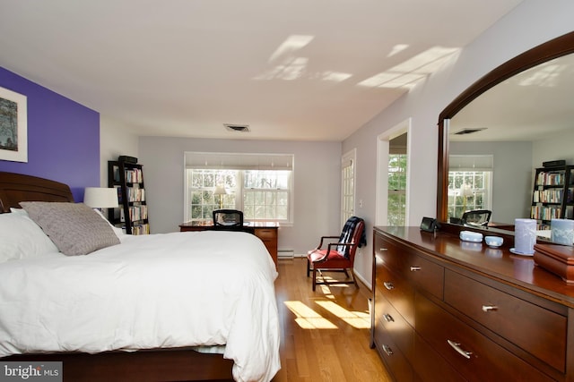 bedroom with baseboard heating, multiple windows, and light hardwood / wood-style flooring