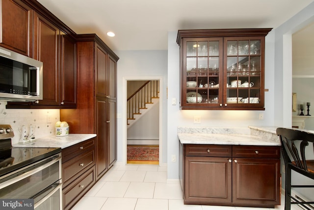 kitchen featuring light stone counters, light tile patterned floors, a baseboard radiator, appliances with stainless steel finishes, and backsplash