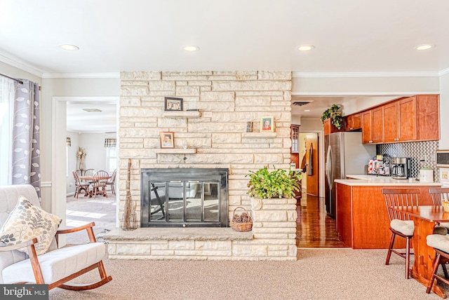 carpeted living room with a stone fireplace and crown molding