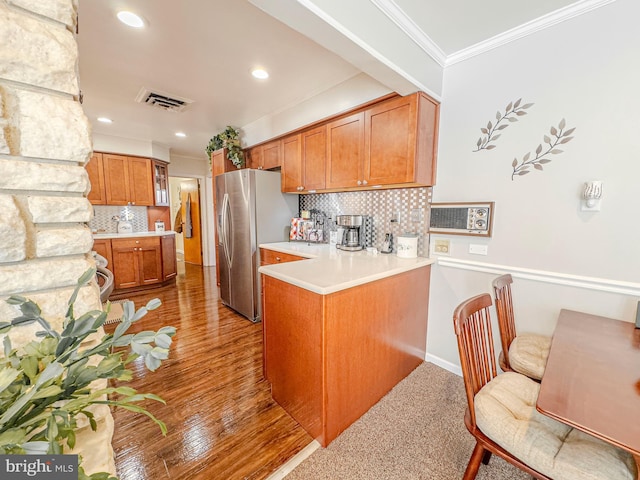 kitchen featuring backsplash, stainless steel refrigerator, kitchen peninsula, and crown molding