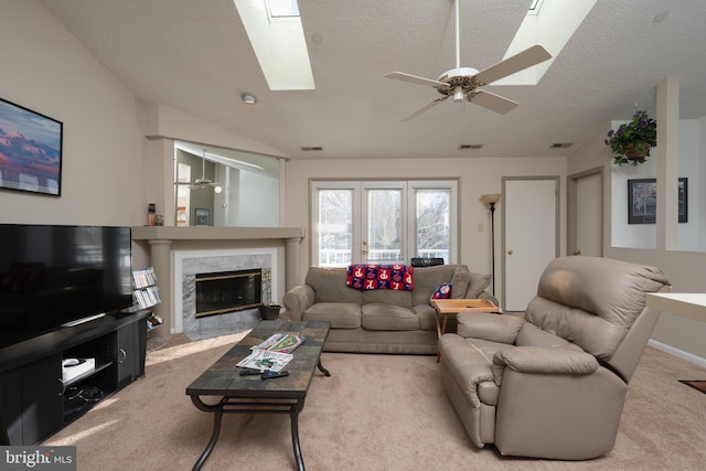 carpeted living room featuring a textured ceiling, vaulted ceiling with skylight, ceiling fan, and a premium fireplace