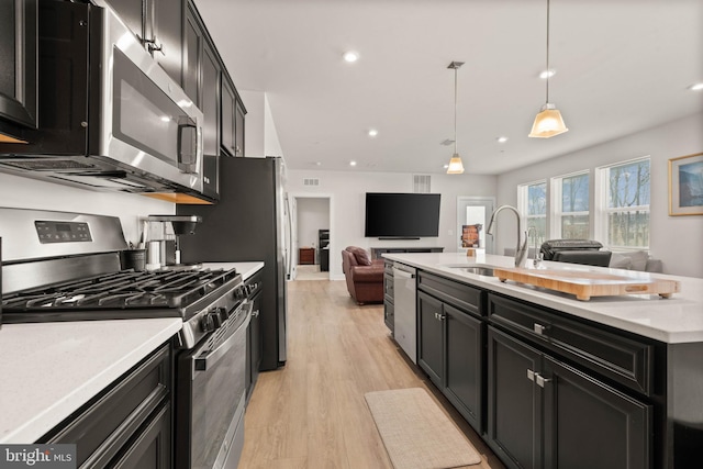 kitchen with stainless steel appliances, hanging light fixtures, sink, and light hardwood / wood-style floors