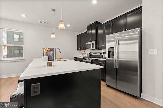 kitchen featuring appliances with stainless steel finishes, light hardwood / wood-style flooring, hanging light fixtures, and a center island with sink