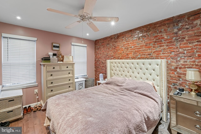 bedroom with ceiling fan, light hardwood / wood-style floors, and brick wall