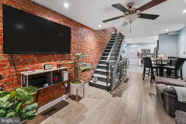 living room with ceiling fan, brick wall, and light hardwood / wood-style flooring