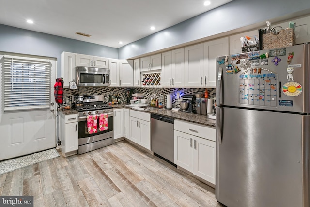 kitchen featuring white cabinetry, light hardwood / wood-style floors, stainless steel appliances, dark stone countertops, and sink