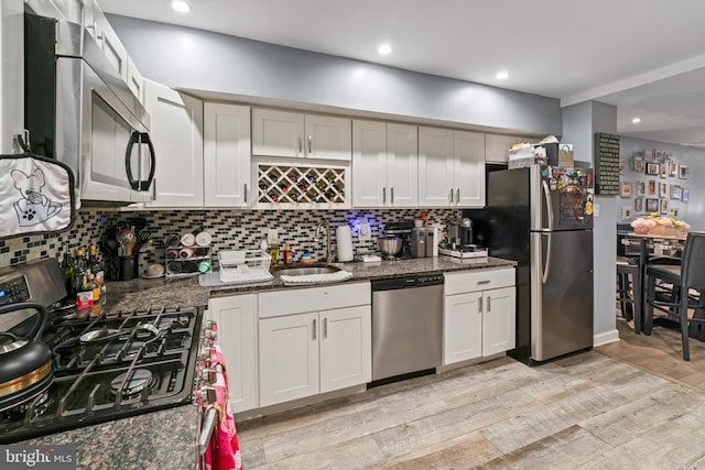 kitchen featuring stainless steel appliances, dark stone countertops, white cabinetry, and sink