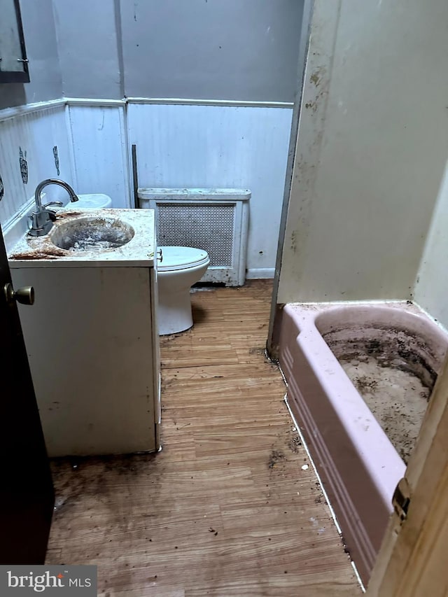 bathroom with toilet, wood-type flooring, radiator heating unit, a bath, and vanity