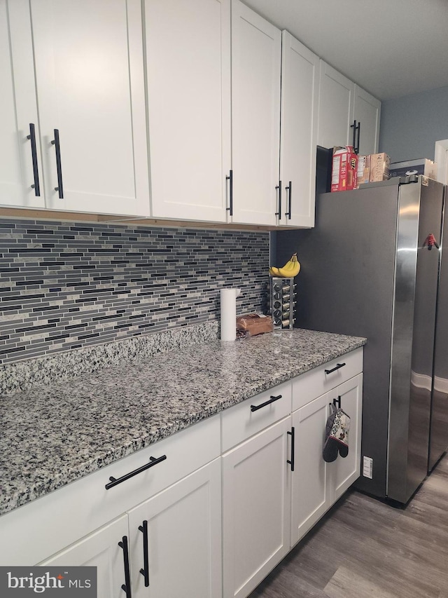 kitchen with light stone countertops, decorative backsplash, white cabinets, dark wood-type flooring, and stainless steel fridge