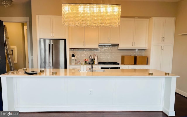 kitchen with a center island with sink, sink, high end fridge, white cabinets, and decorative backsplash