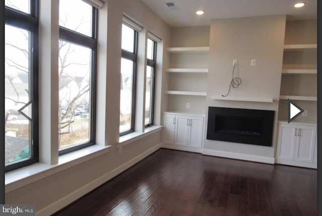 unfurnished living room featuring built in shelves, dark hardwood / wood-style floors, and a healthy amount of sunlight