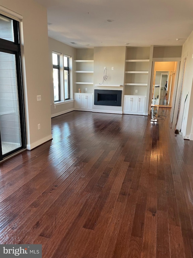 unfurnished living room with dark hardwood / wood-style flooring and built in shelves