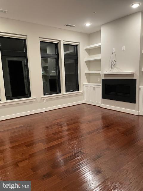 unfurnished living room with dark wood-type flooring and built in features