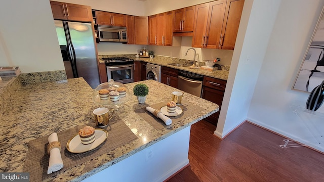 kitchen with dark hardwood / wood-style floors, kitchen peninsula, sink, light stone countertops, and stainless steel appliances