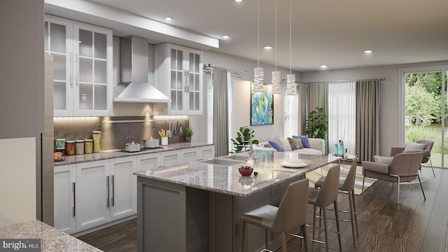 kitchen with dark hardwood / wood-style flooring, wall chimney exhaust hood, backsplash, white cabinetry, and an island with sink