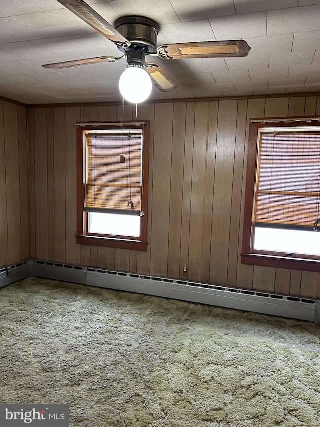 carpeted empty room with ceiling fan, wooden walls, and a wealth of natural light