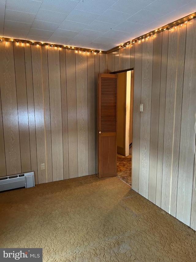 empty room featuring a baseboard heating unit, carpet floors, and wooden walls