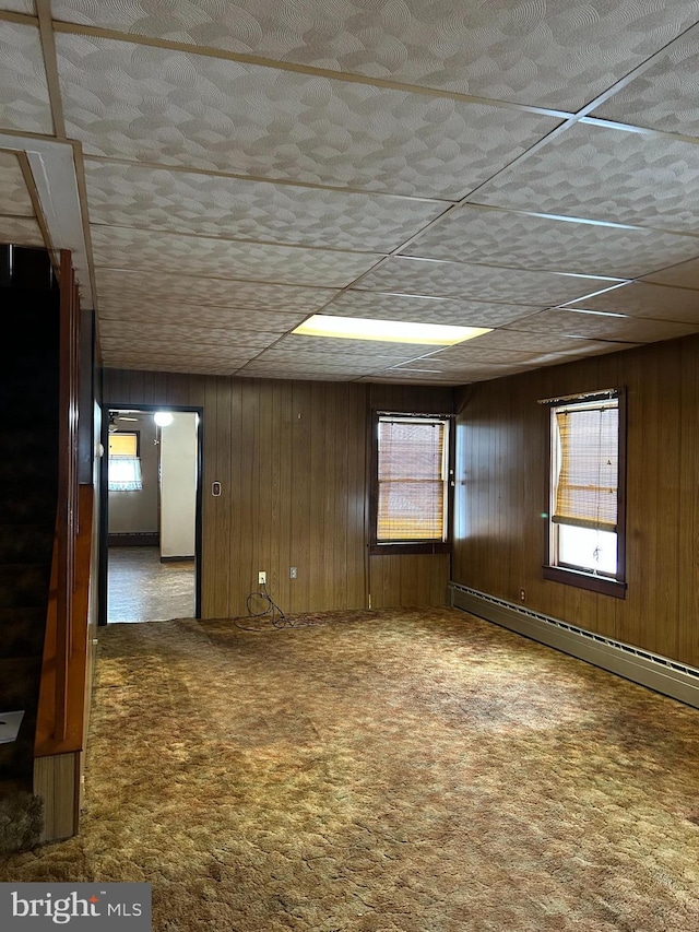 carpeted empty room featuring baseboard heating and wood walls