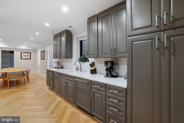 kitchen with light stone counters, sink, ornamental molding, and light parquet flooring