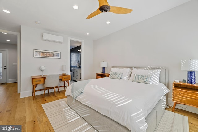 bedroom with ceiling fan, a wall mounted air conditioner, ensuite bathroom, and light hardwood / wood-style flooring