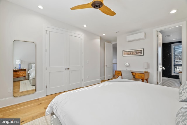 bedroom featuring ceiling fan, a closet, a wall unit AC, and light hardwood / wood-style flooring