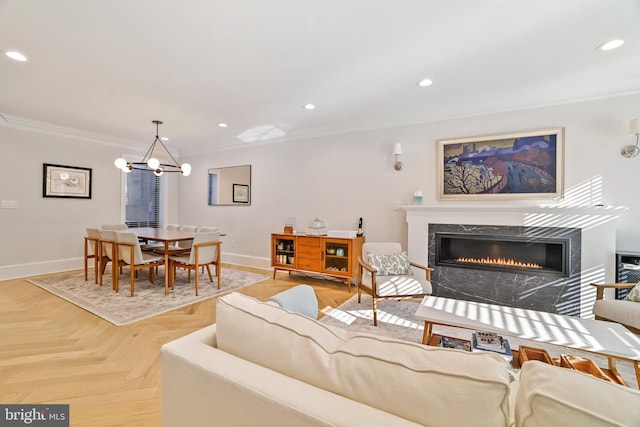 living room with light parquet floors, ornamental molding, a premium fireplace, and a notable chandelier