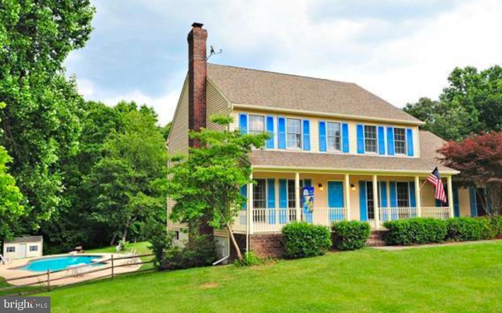 colonial house with a storage shed, covered porch, and a front lawn