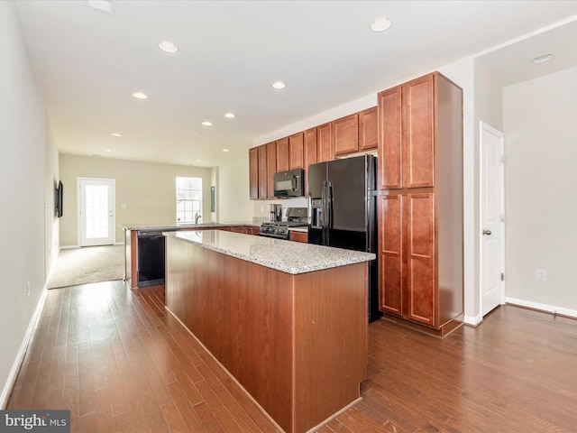 kitchen featuring kitchen peninsula, wood-type flooring, sink, light stone countertops, and black appliances