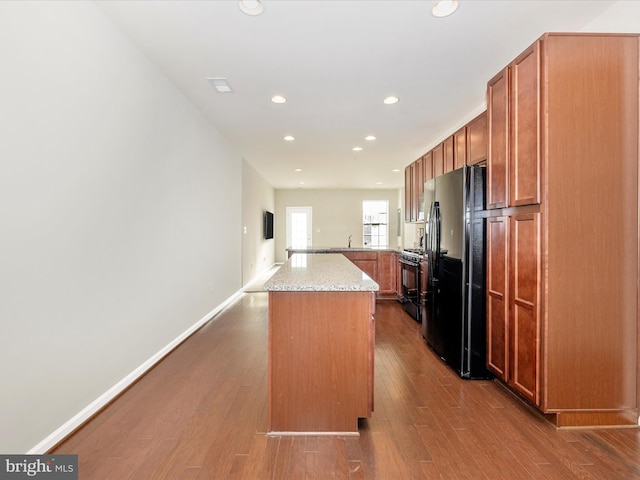 kitchen featuring a center island, black appliances, hardwood / wood-style flooring, kitchen peninsula, and light stone counters