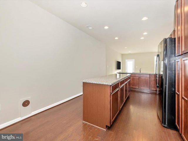 kitchen featuring light stone countertops, a kitchen island, dark wood-type flooring, sink, and black fridge