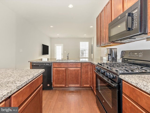 kitchen featuring sink, black appliances, light wood-type flooring, and light stone countertops