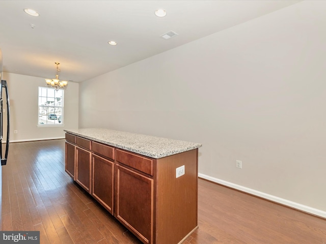 kitchen with light stone countertops, pendant lighting, a center island, dark wood-type flooring, and a notable chandelier