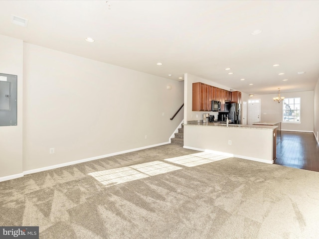 unfurnished living room featuring electric panel, light colored carpet, and a notable chandelier