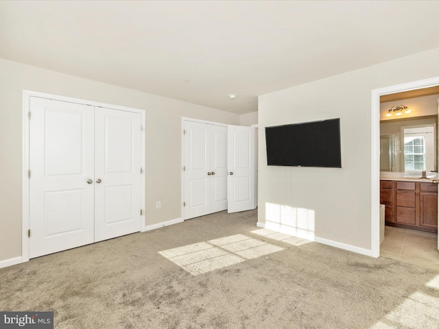 unfurnished bedroom with light carpet, multiple closets, and ensuite bath