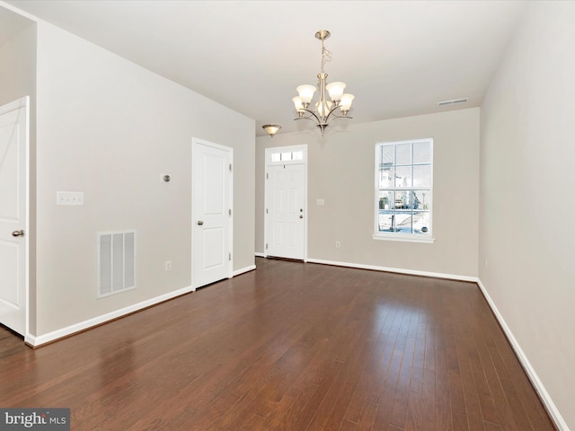 spare room with dark wood-type flooring and a notable chandelier