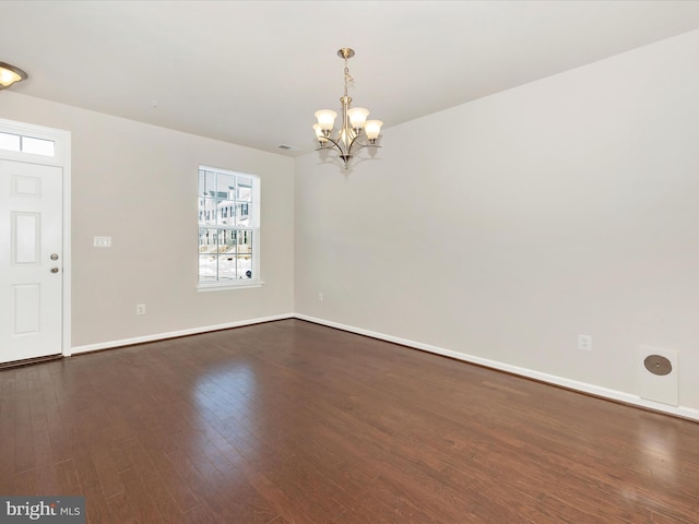 spare room with dark wood-type flooring and an inviting chandelier