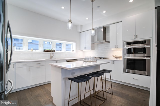 kitchen featuring appliances with stainless steel finishes, white cabinetry, sink, and wall chimney range hood