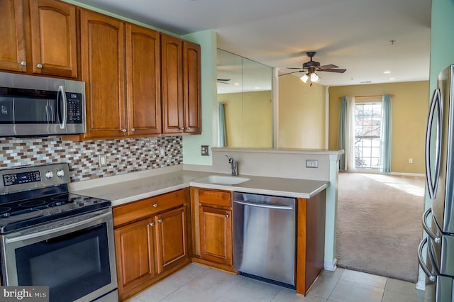 kitchen with sink, backsplash, kitchen peninsula, stainless steel appliances, and light carpet