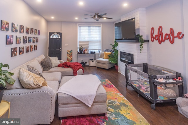 living room with a fireplace, dark wood-type flooring, and ceiling fan