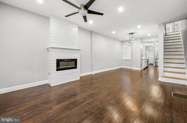 unfurnished living room with dark wood-type flooring, a large fireplace, and ceiling fan