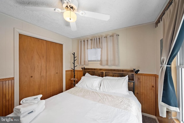 bedroom featuring ceiling fan, wooden walls, a textured ceiling, and a closet