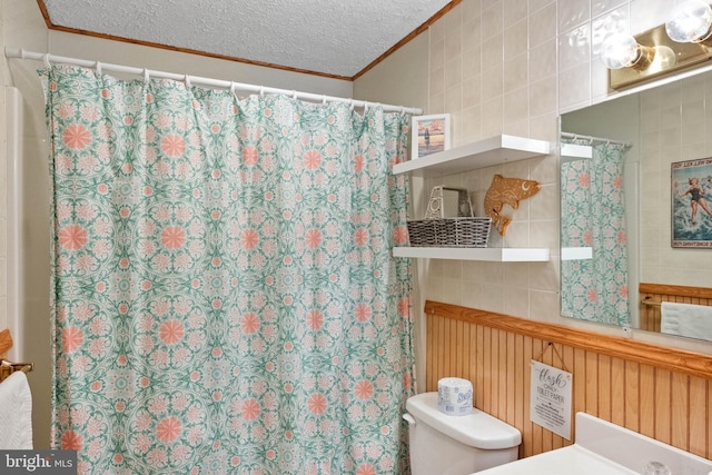 bathroom with ornamental molding, toilet, a textured ceiling, and tile walls