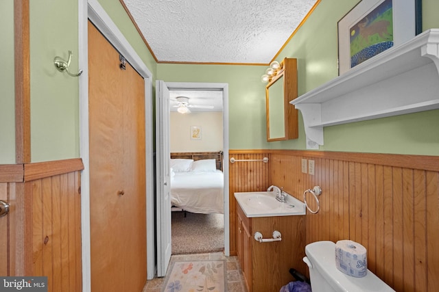 bathroom with wooden walls, ornamental molding, vanity, toilet, and a textured ceiling