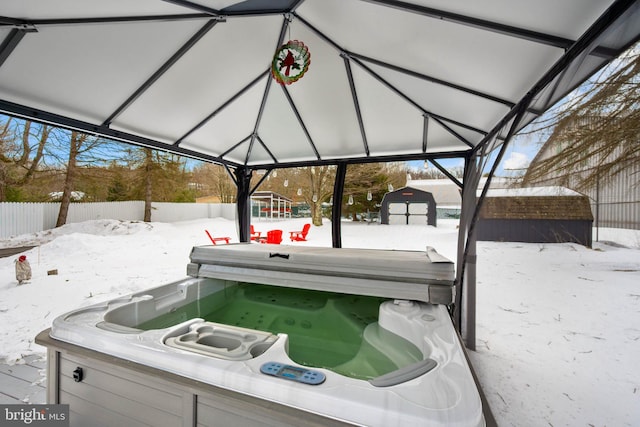 snow covered patio with a storage shed and a hot tub