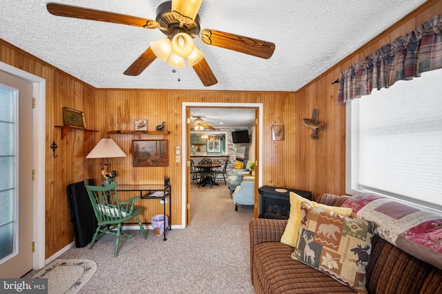 living room with crown molding, ceiling fan, wooden walls, carpet, and a textured ceiling