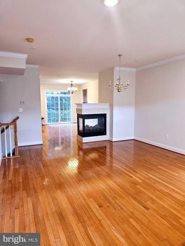 unfurnished living room with a multi sided fireplace, wood-type flooring, an inviting chandelier, and ornamental molding