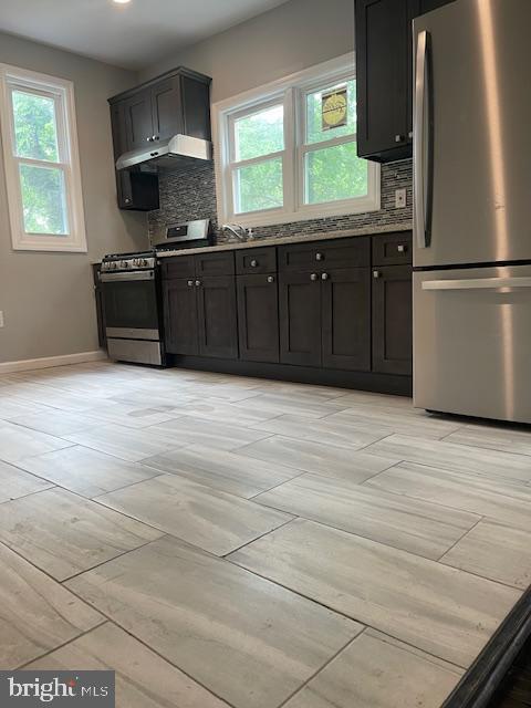 kitchen with backsplash, a wealth of natural light, light stone counters, and stainless steel appliances