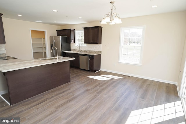 kitchen featuring stainless steel appliances, light wood-type flooring, dark brown cabinets, pendant lighting, and sink