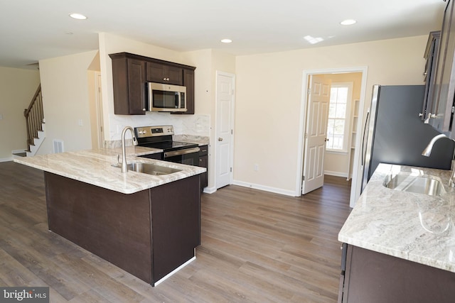 kitchen with sink, dark wood-type flooring, appliances with stainless steel finishes, dark brown cabinets, and light stone counters